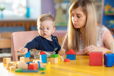Cute woman teacher and child playing educational toys at kindergarten or nursery roomの写真素材