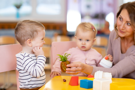 Preschool teacher with children boy and girl playing with colorful toys at kindergartenの写真素材