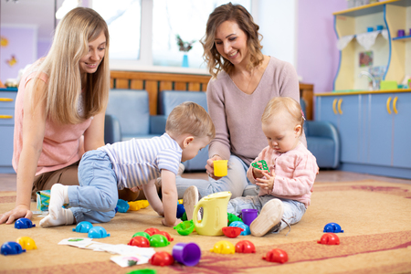 Babies toddlers crawling and having fun on floor in nursery. Mothers play with children in day care centre.の写真素材