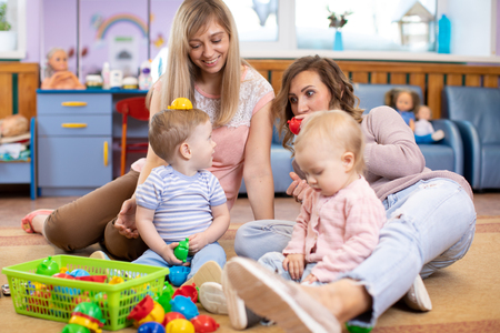 Two children boys with their moms playing with lots of colorful plastic blocks constructor sitting on a floor indoorの写真素材