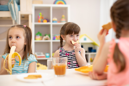 Funny children girls eating healthy food. Kids lunch at daycare or kindergarten.の写真素材