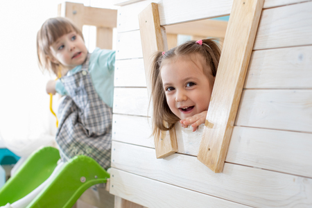 Cute child girl looks out the window of wooden toy house, and smiles.の写真素材