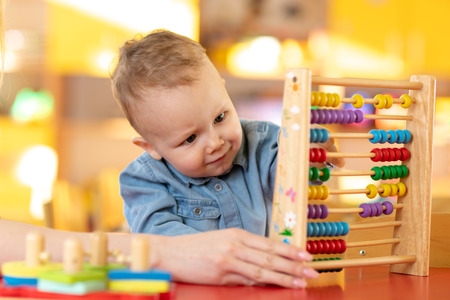 Nursery baby boy playing with toy abacus in kindergarten