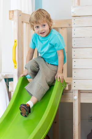 Kid boy playing fun in the playroom, coming down from the green hillの写真素材