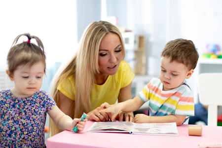 Day care worker with children reading a book in kindergartenの写真素材