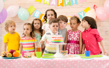 Group of children blowing candles on cake at birthday party