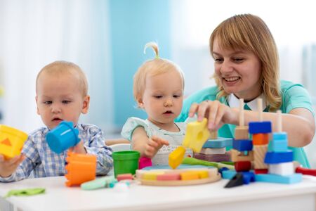 Nursery teacher looking after children in daycare. Little kids toddlers play together with developmental toys.の写真素材