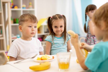 Kids have a lunch in daycare centre. Children eat fresh fruits in kindergartenの写真素材