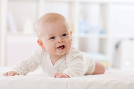 infant baby five months age lying on belly in white sunny nurseryの写真素材