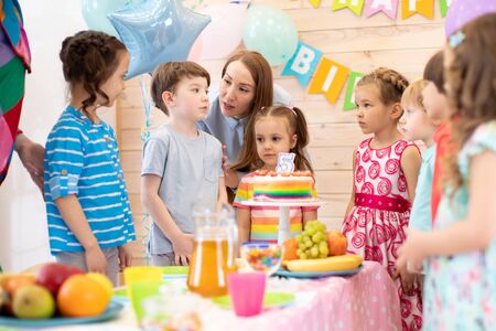 Group of adorable kids gathered around festive table. Birthday party for preschoolersの写真素材