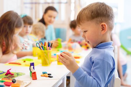 Child boy and group of kids working with colorful clay toy in nursery. Creative child molding in kindergarten. Preschoolers play with plasticine or dough.