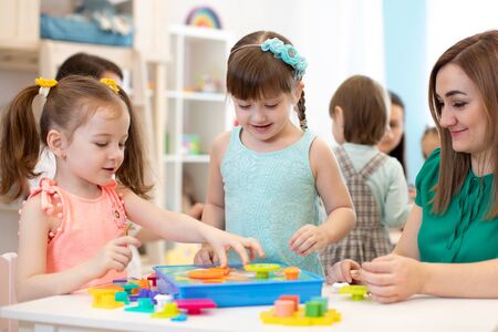 Kindergarten teacher and children playing toy sorter in daycare centreの写真素材