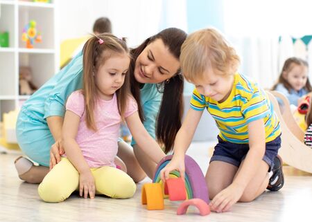 Preschool children and kindergarten teacher playing with wooden toysの写真素材