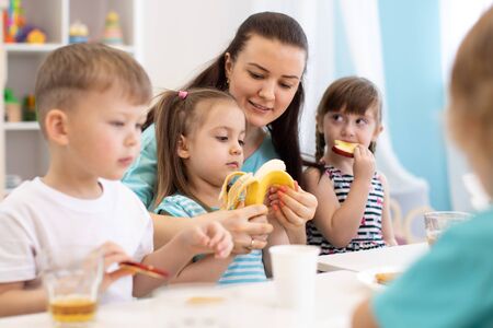 kindergarten teacher and preschoolers children having break for fruits and vegetablesの写真素材