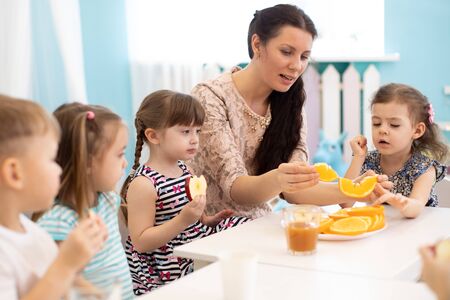 kindergarten teacher and preschoolers children have break for fruits and vegetablesの写真素材