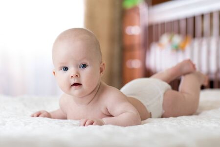 Baby infant wearing diaper in bedroom. Newborn child relaxing in nursery. Newborn kid lying on tummyの写真素材