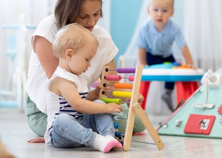 Kids playing on floor with educational toys in kindergarten. Children have fun in nursery or daycare. Babies with teacher in crecheの写真素材