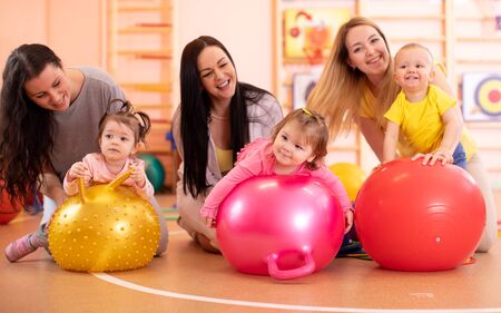 Group of young mothers and their kids doing yoga exercises on gymnastic balls at fitness gymの写真素材
