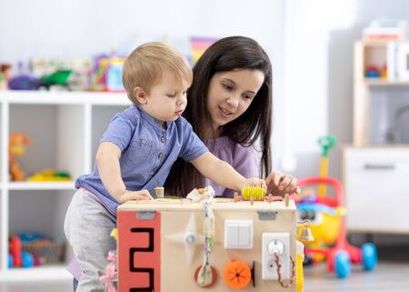 Cute toddler baby playing with busyboard. Mother teaching child in nursery or daycareの写真素材