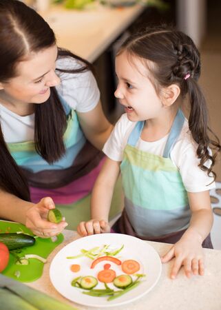 Happy mother and her kid enjoy making healthy meal together at their kitchenの写真素材