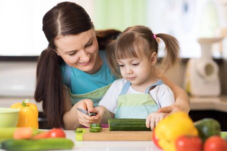 Mom with her daughter in kitchen preparing healthy food with fresh vegetables, home parenting lifestyleの写真素材