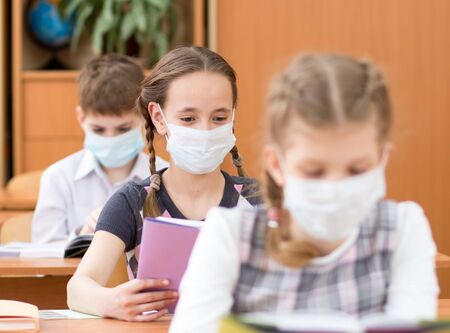 Schoolkids with medicine mask on faces against virus in classroomの写真素材