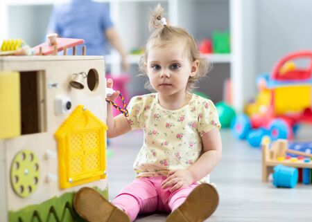 Cute toddler baby playing with busy board in daycare. Childrens educational toys.