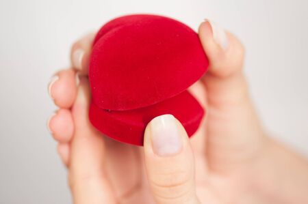 Red gift box in the form of heart with a ring inside in female hands on a white background shot with...