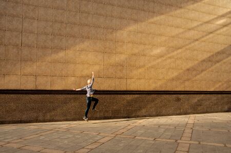 blonde woman with short haircut in jeans runs over a big wall on a city street in the summer on a sunny day, Chelyabinsk, Russia -17 August, 2016のeditorial素材