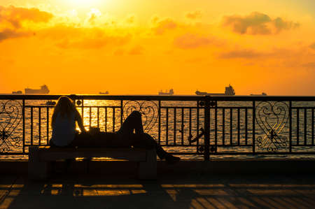 silhouettes of a couple against the background of the sea at sunset in summerの写真素材