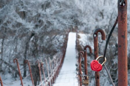red lock in the form of a heart on a suspension bridge across the river in winter