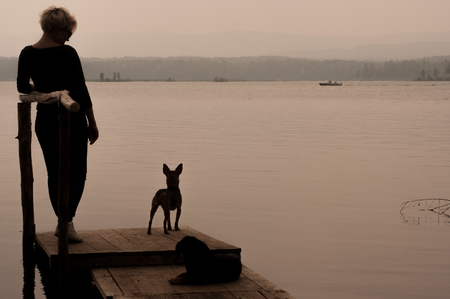 Lake Argazi, Chelyabinsk Region, Russia July 23, 2016: Girl with two dogs are standing on the pier by the lake waiting for late eveningのeditorial素材