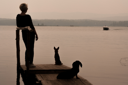 Lake Argazi, Chelyabinsk Region, Russia July 23, 2016: Girl with two dogs are standing on the pier by the lake waiting for late eveningのeditorial素材