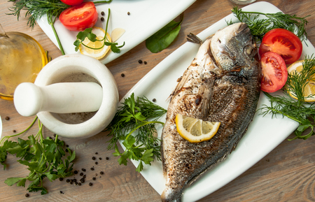 Food photo Food photo Fish Dorada grilled served in a white plate with greens, vegetables and lemon close-upの写真素材