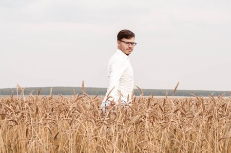 Men in a white shirt walks on a wheat field in the summer on a sunny dayの写真素材