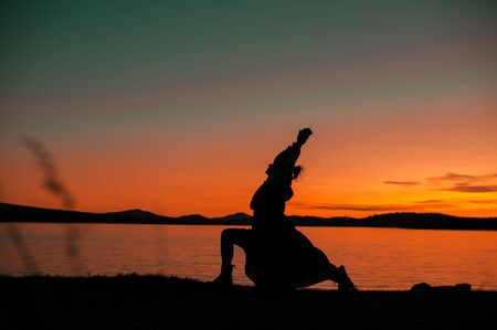 Silhouette of a girl in a dress in a yoga pose on the background of a beautiful orange sunset on the...