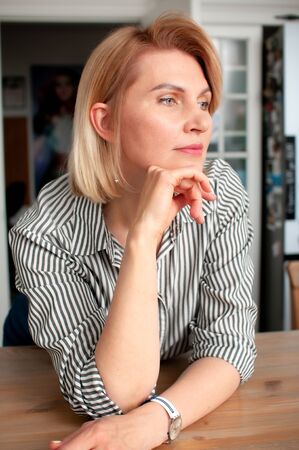 Close-up portrait of a blonde woman with a bobcare haircut in a shirt and jeans indoors in everyday lifeの写真素材