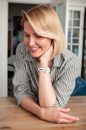 Close-up portrait of a blonde woman with a bobcare haircut with a smile on her face in a shirt and jeans indoorsの写真素材