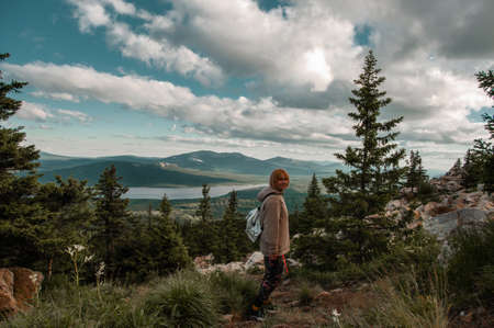 tourist woman with a backpack on the background of a beautiful landscape with a mountain range on the nature and blue sky with white clouds on the forest meadows and lake in summer Russia, Chelyabinsk region, Zyuratkul Rangeの写真素材