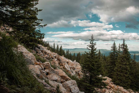 Beautiful landscape with a mountain range on a blue sky with white clouds on the forest meadows and...