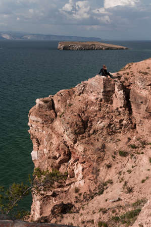 Woman sits on the top of a rock and looks at a picturesque view of Lake Baikal on a summer dayの写真素材