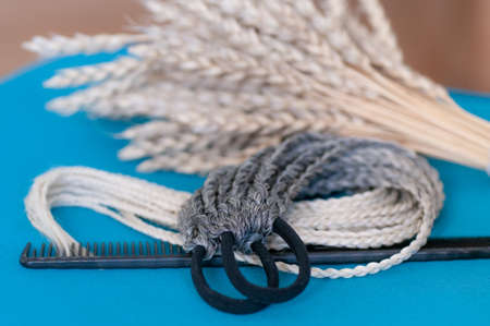 Decorative hair accessory of natural light color, elastic band with small colored braids, handmade close-upの写真素材