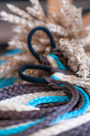 Decorative hair accessory of brown blue color, elastic band with small colored braids, handmade close-upの写真素材