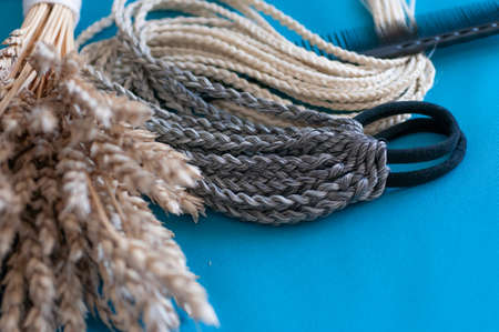 Decorative hair accessory of natural light color, elastic band with small colored braids, handmade close-upの写真素材