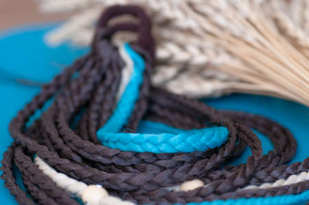 Decorative hair accessory of brown blue color, elastic band with small colored braids, handmade close-upの写真素材