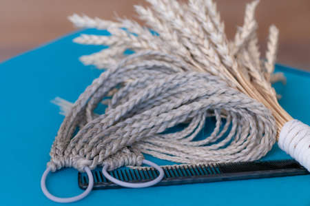 Decorative hair accessory of natural light color, elastic band with small colored braids, handmade close-upの写真素材