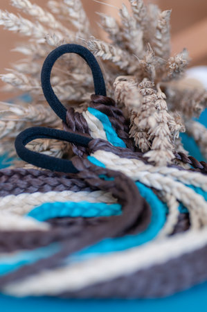 Decorative hair accessory of brown blue color, elastic band with small colored braids, handmade close-upの写真素材