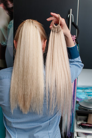 Blonde woman with long hair from the back demonstrates an artificial ponytail on her own hair indoorsの写真素材