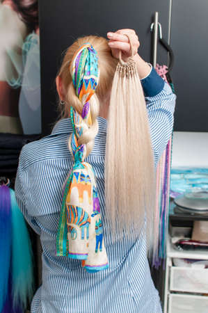 Blonde woman with long hair from the back demonstrates an artificial ponytail on her own hair...