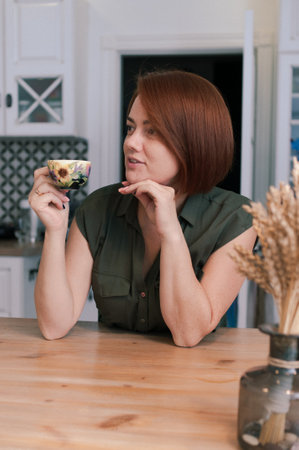Portrait of a woman with bob haircut and red natural hair in everyday life at home with a cup of tea in her handsの写真素材